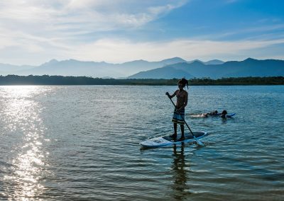 Rastaman doing stand up paddling on river in Barra do Una, Brazil