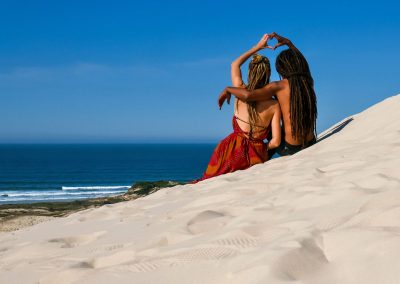Rasta couple looking out to ocean and forming heart on Dunas da Ribanceira in Imbituba, Brazil