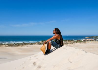 Rastaman sitting in Dunas da Ribanceira with ocean in background in Imbituba, Brazil