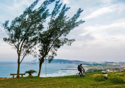 Rasta girl riding bike overlooking ocean and port of Imbituba, Brazil